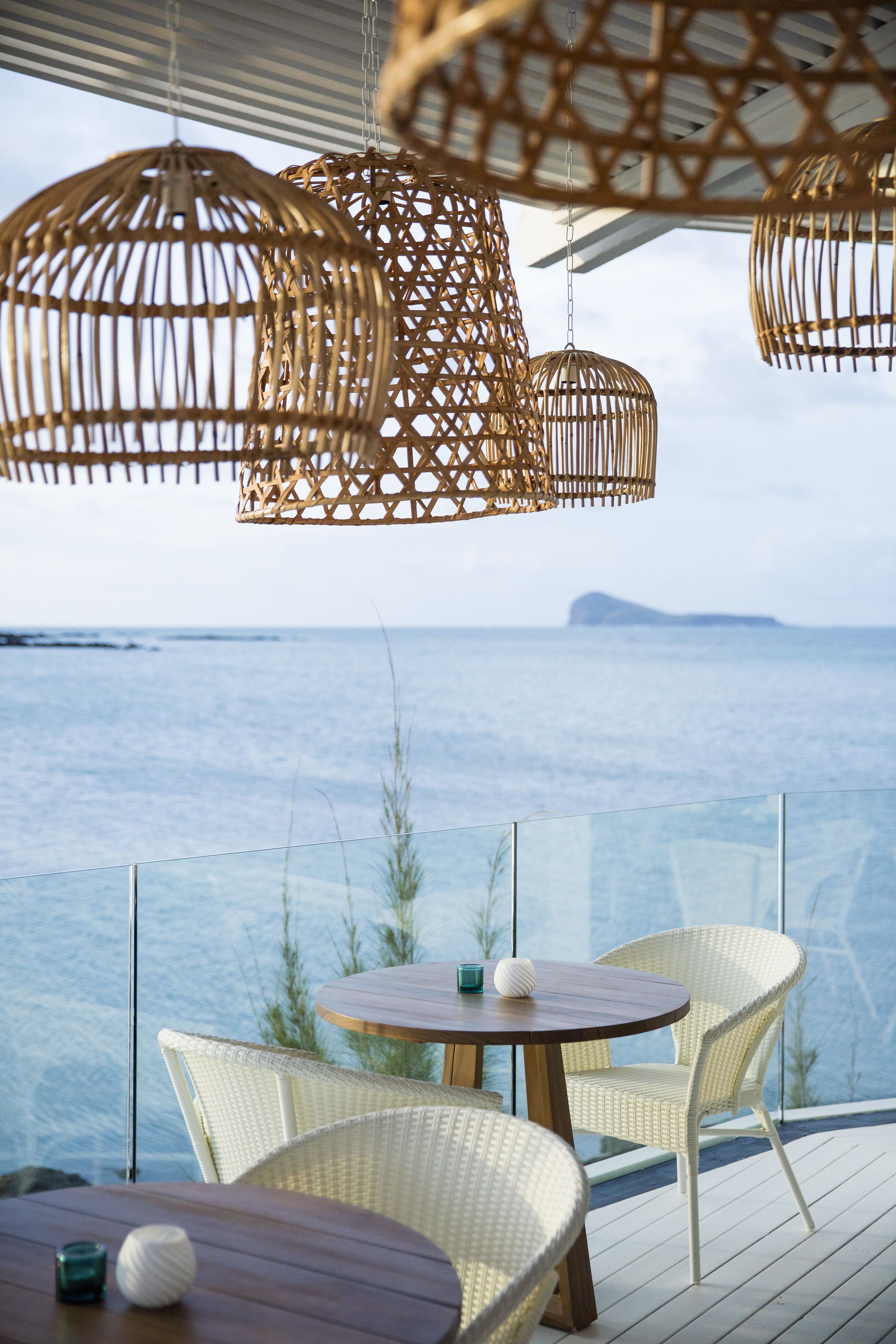 A seaside terrace with wicker furniture and hanging wicker lamps.
