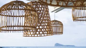 A seaside terrace with wicker furniture and hanging wicker lamps.