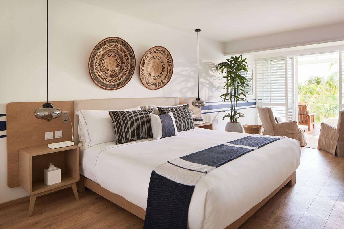A modern bedroom with a large bed, bedside tables, a bedside lamp, and a potted plant.