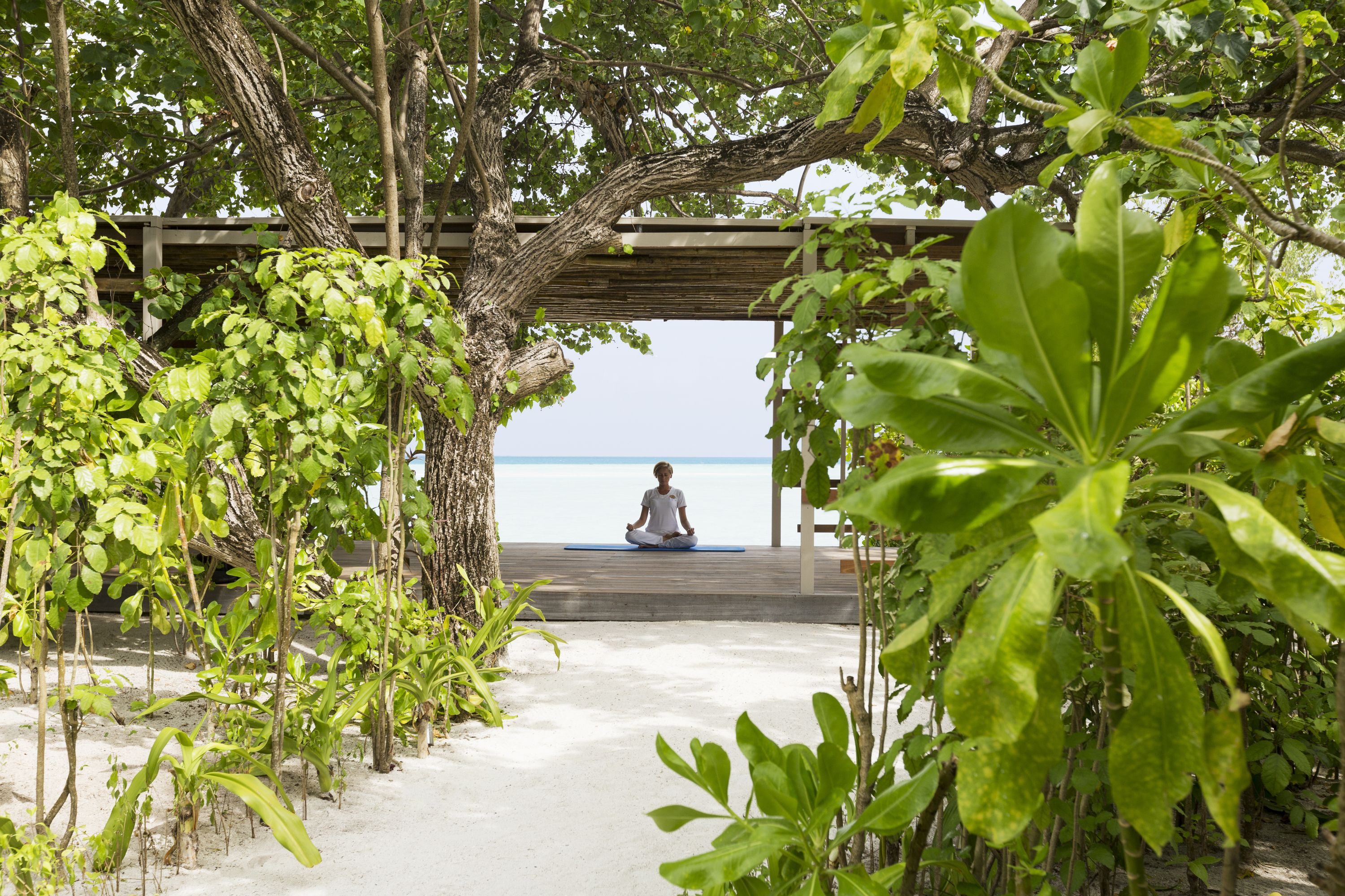 A person meditating on a wooden platform with a view of the sea.