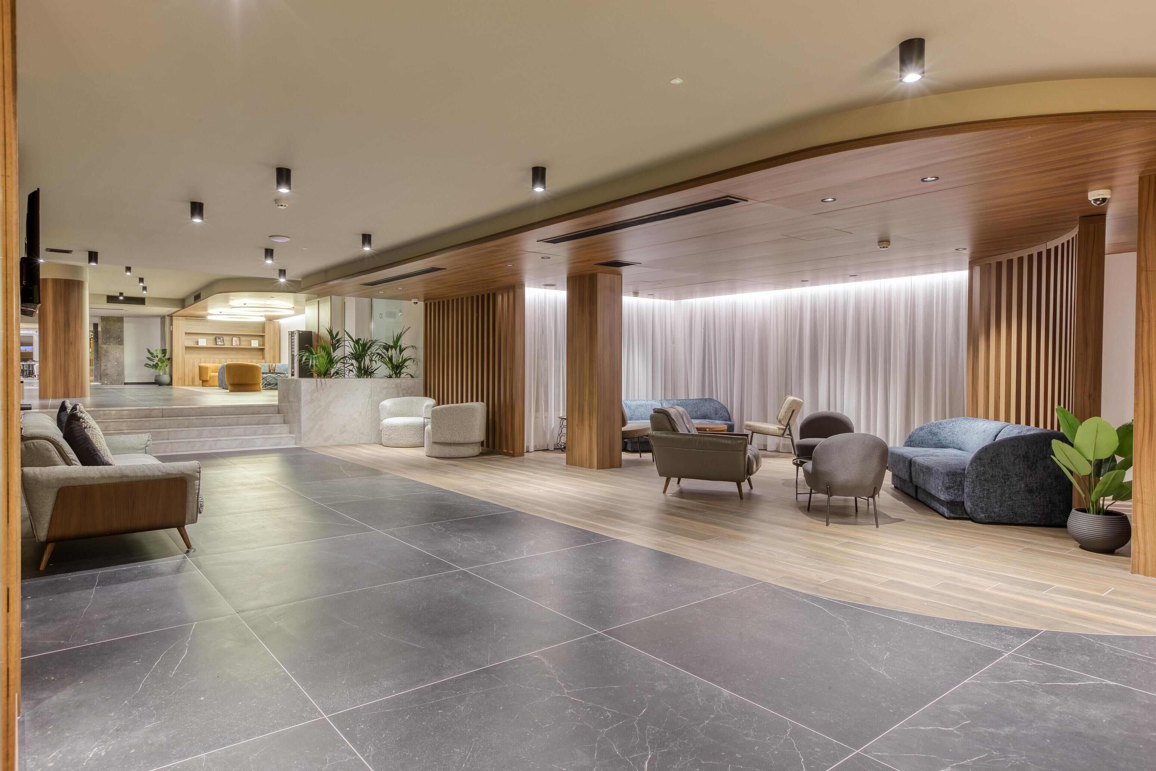 En moderne lobby med reception, siddeområde og trappe til en etage ovenover.