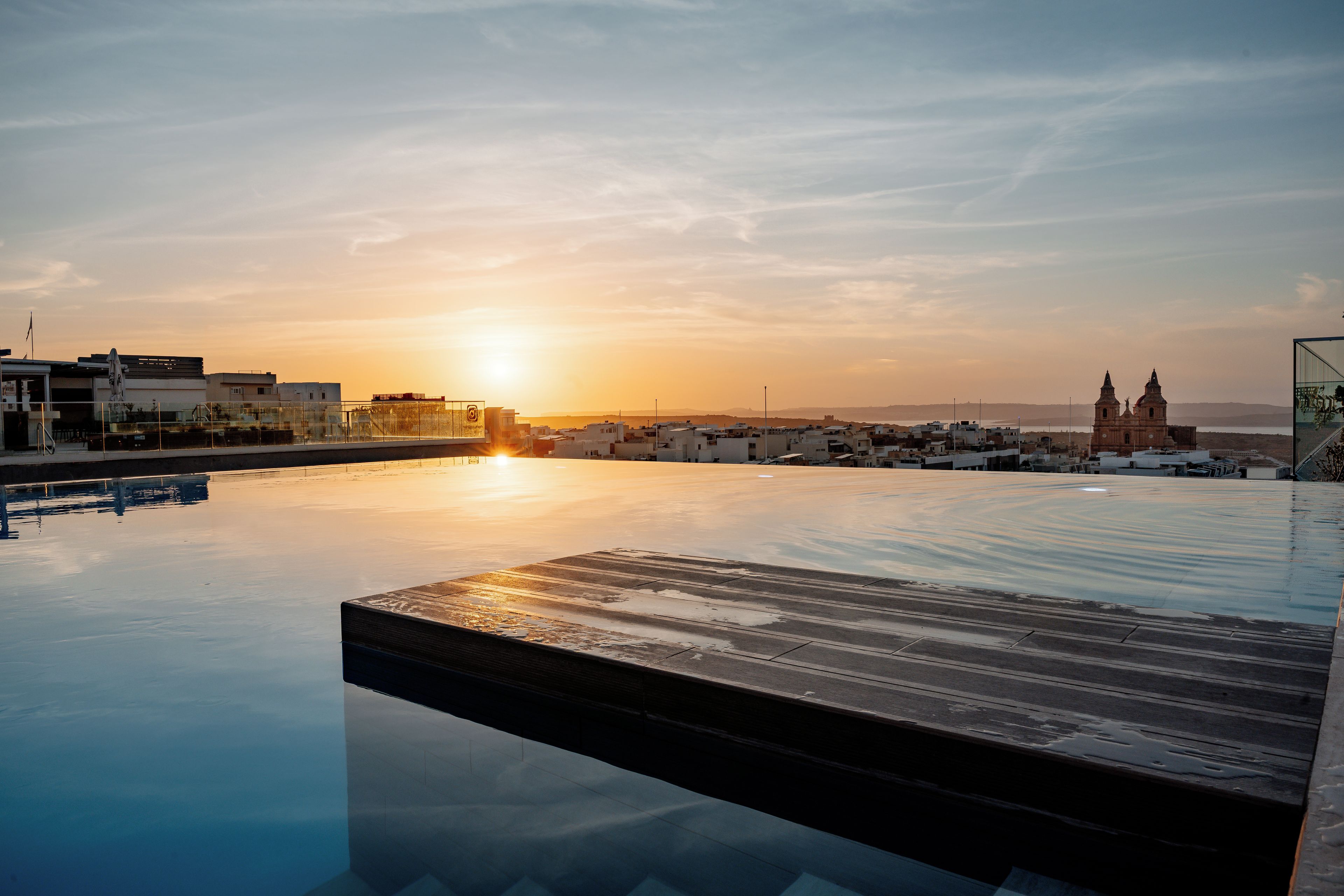 Una piscina infinita con vistas a un paisaje urbano y una iglesia al atardecer.