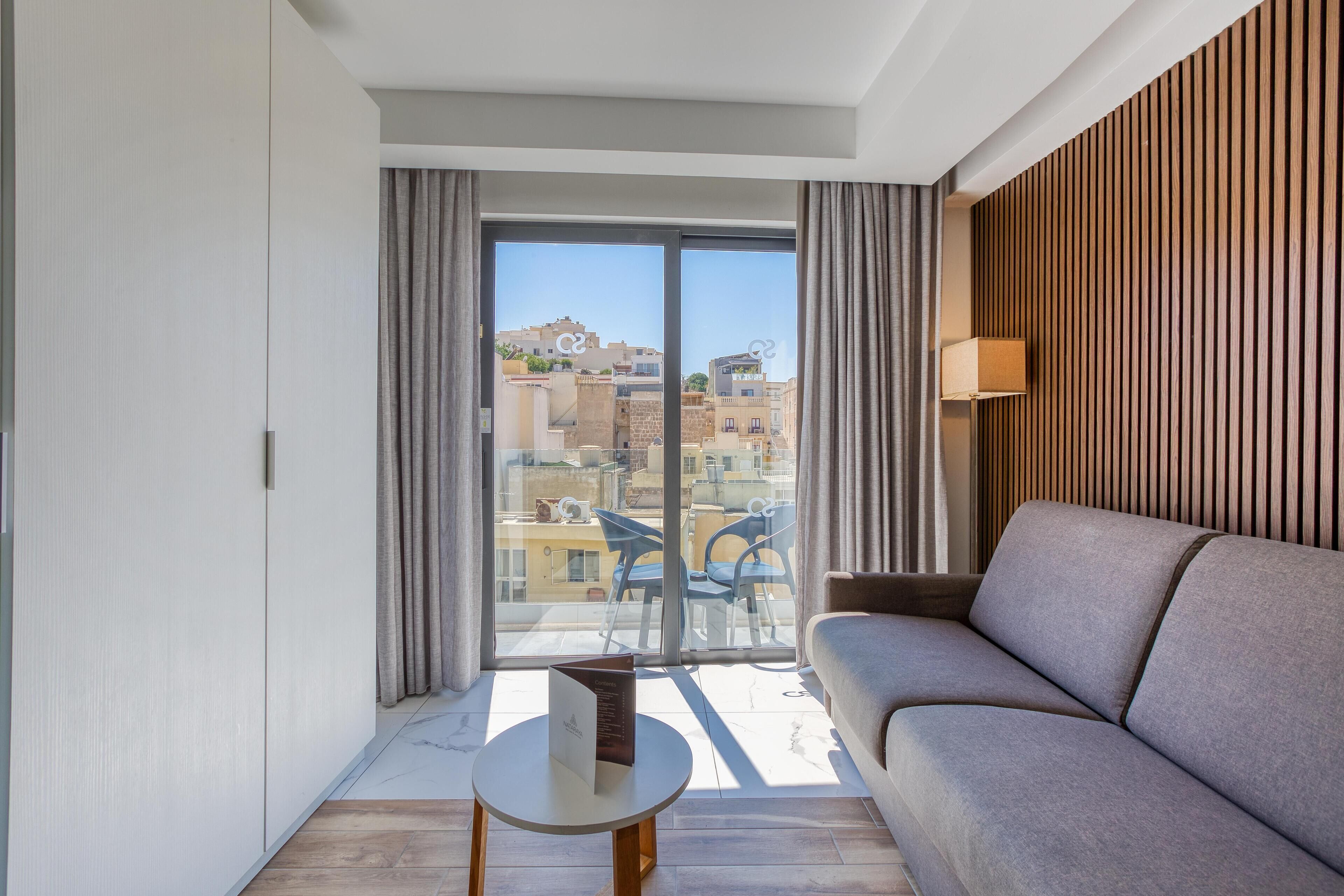A modern living room with a sofa, a small table, and a view of the city through large sliding doors.