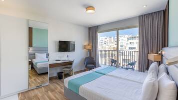 Habitación de hotel con una cama grande, un escritorio, una silla, un televisor y un balcón con vistas a edificios.