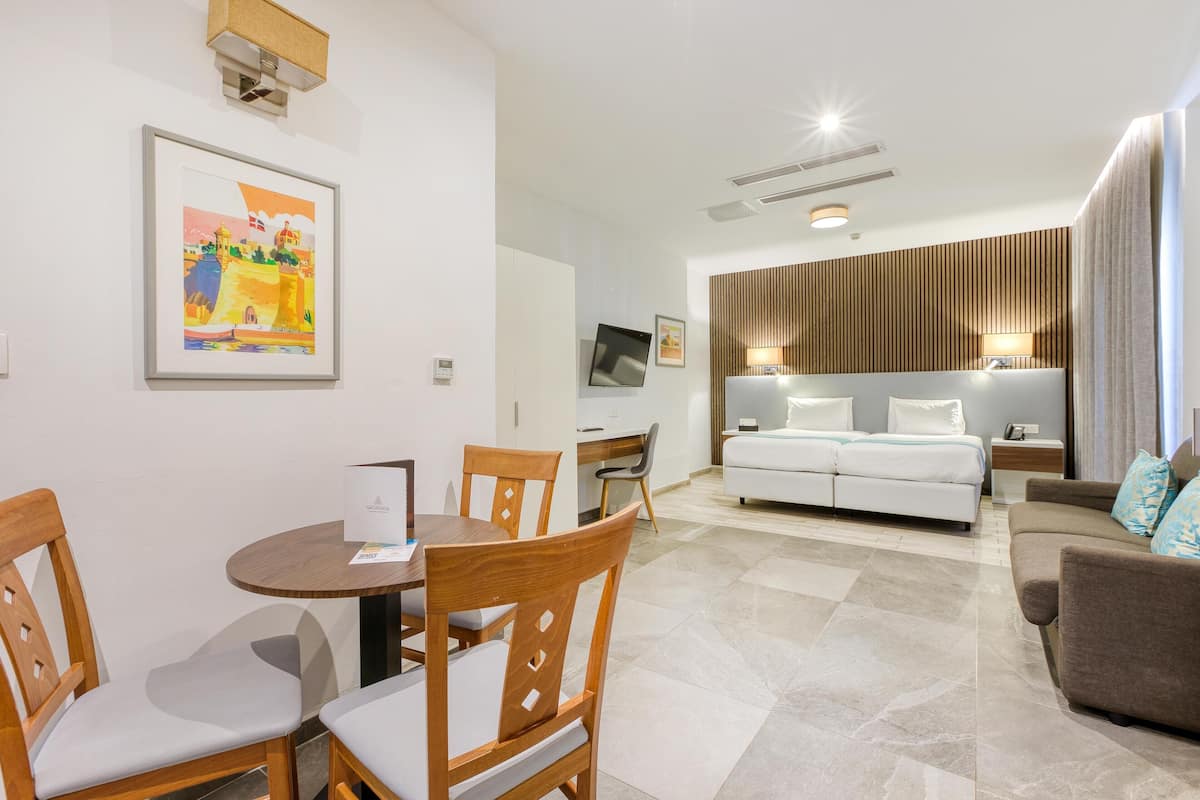 Quarto de hotel moderno com área de refeições, sofá, televisão e cama.