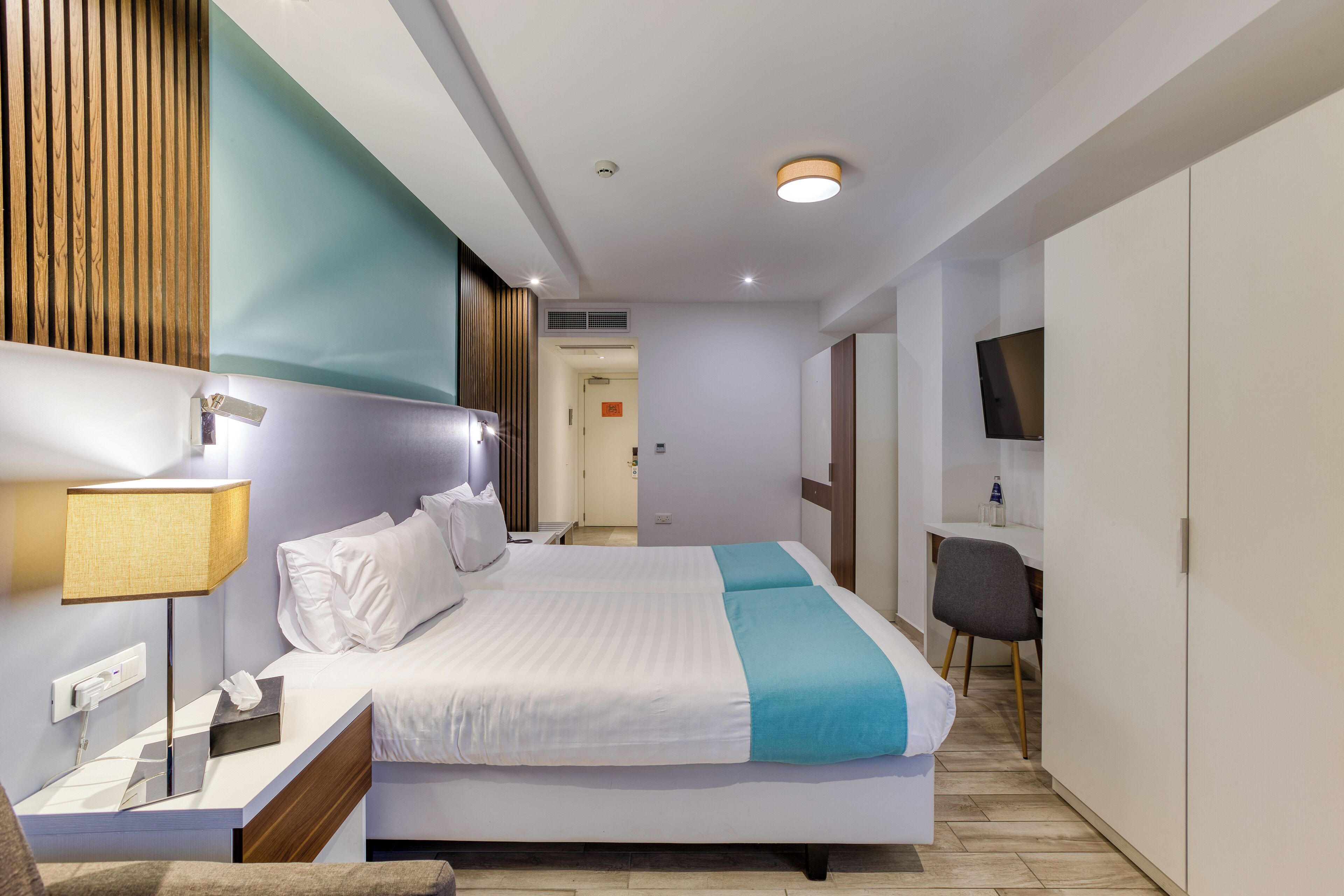 Ein modernes Hotelzimmer mit einem großen Bett, einem Nachttisch mit Lampe, einem Fernseher und einem Kleiderschrank.