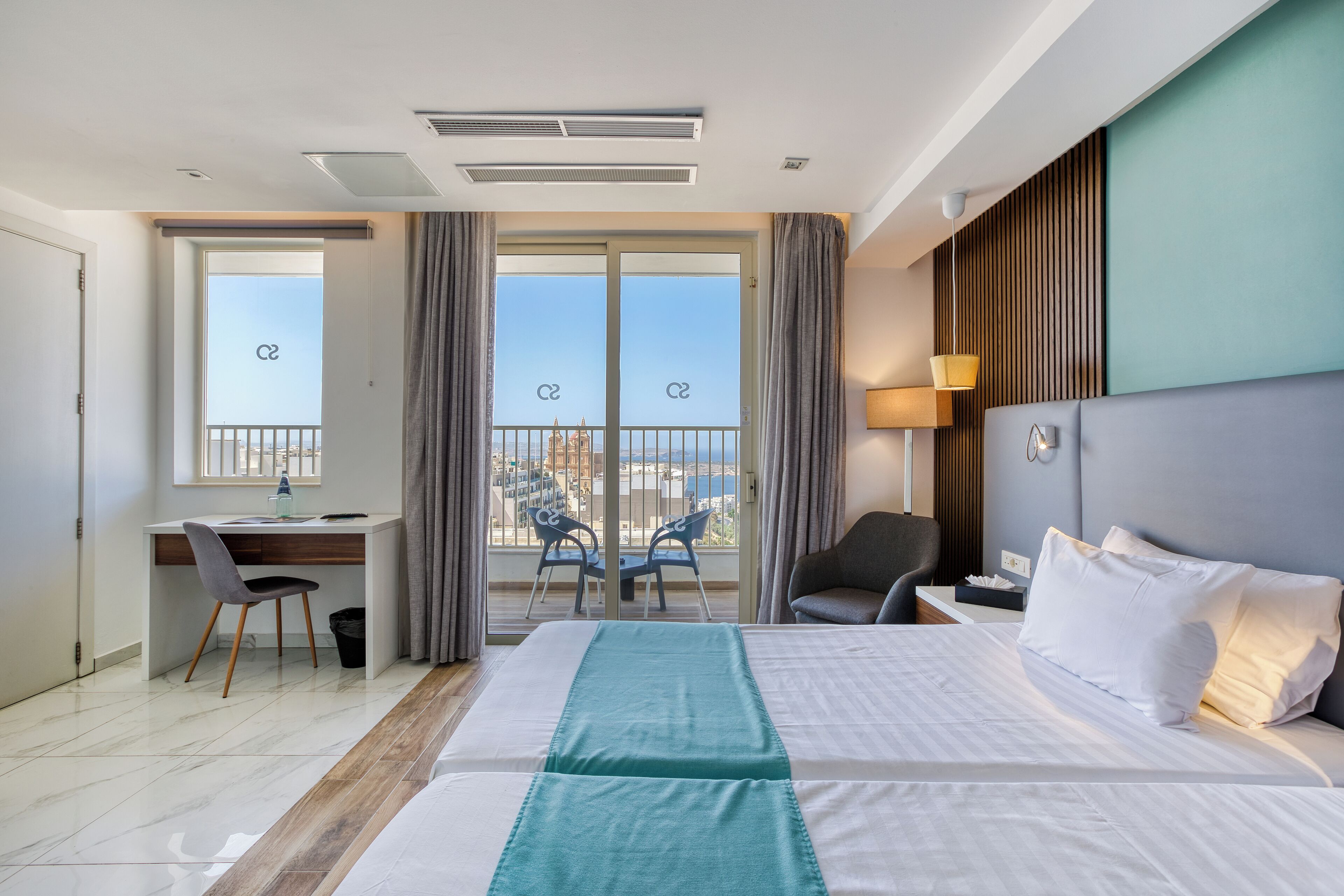 Een hotelkamer met een groot bed, een bureau, een stoel en een balkon met uitzicht.