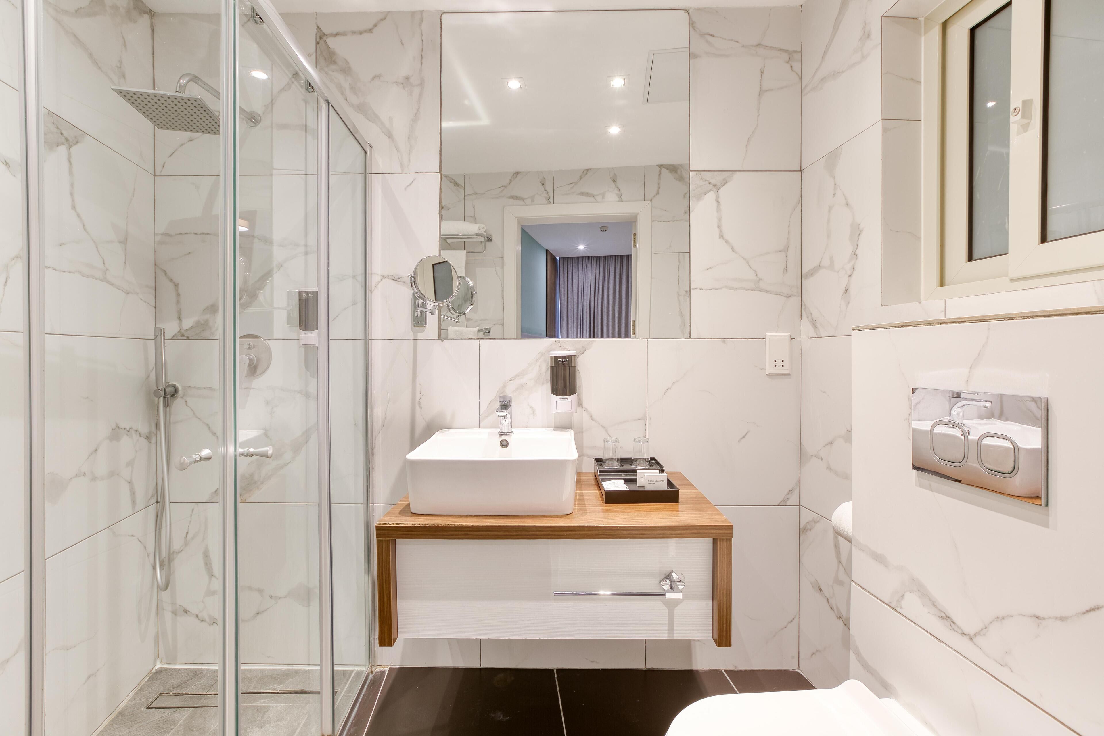 A modern bathroom with a glass-enclosed shower, a wooden vanity with a white sink, and a large mirror.
