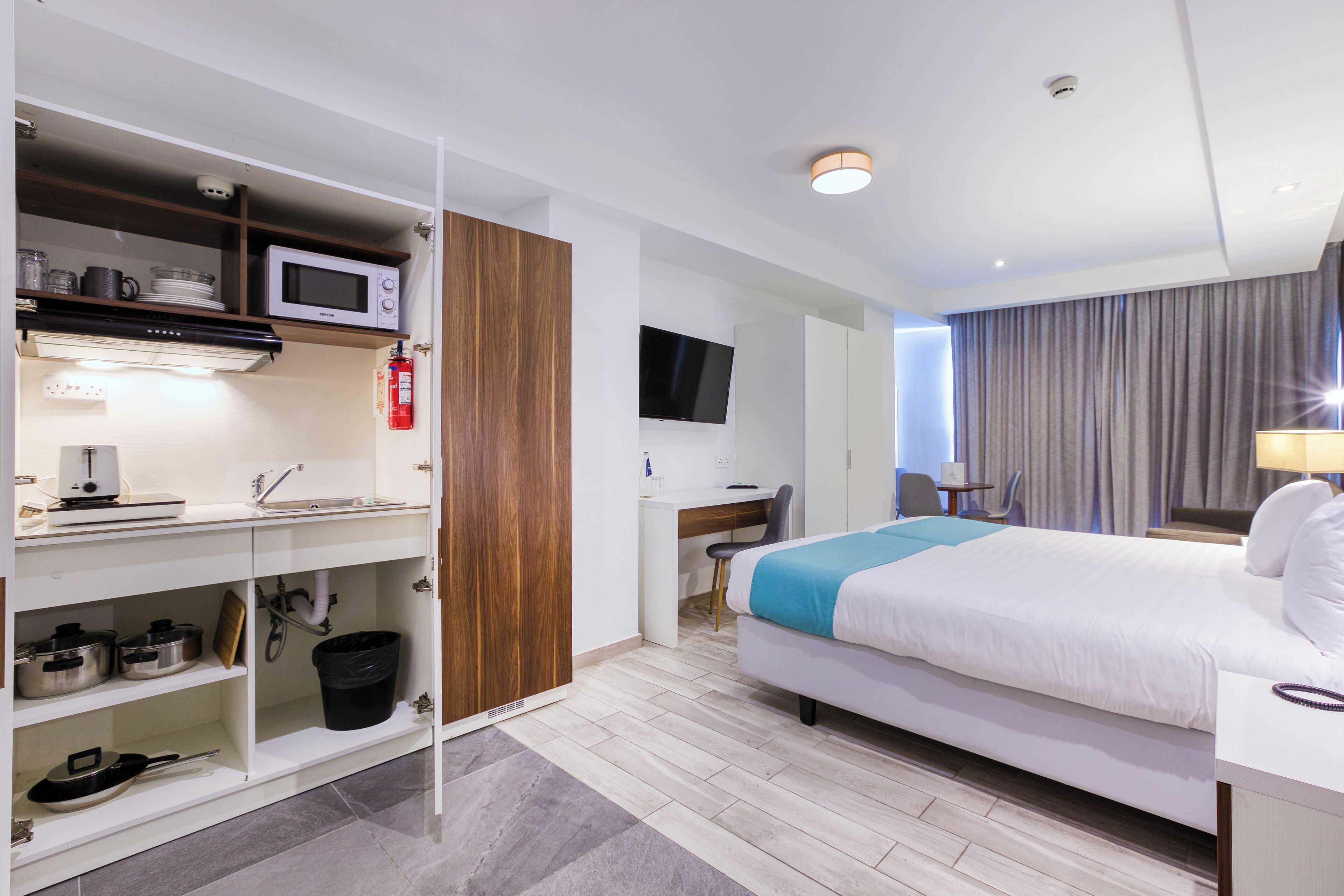 Una habitación de hotel con cama, escritorio, microondas, televisión y armario.
