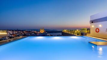 Una piscina sul tetto con vista sulla città, un galleggiante appeso al muro e un tramonto sullo sfondo.