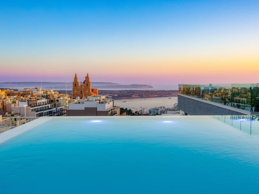 Una piscina infinita en la azotea con vistas a un paisaje urbano costero, destacando una iglesia y edificios modernos.