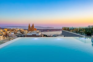 Una piscina infinita en la azotea con vistas a un paisaje urbano costero, destacando una iglesia y edificios modernos.