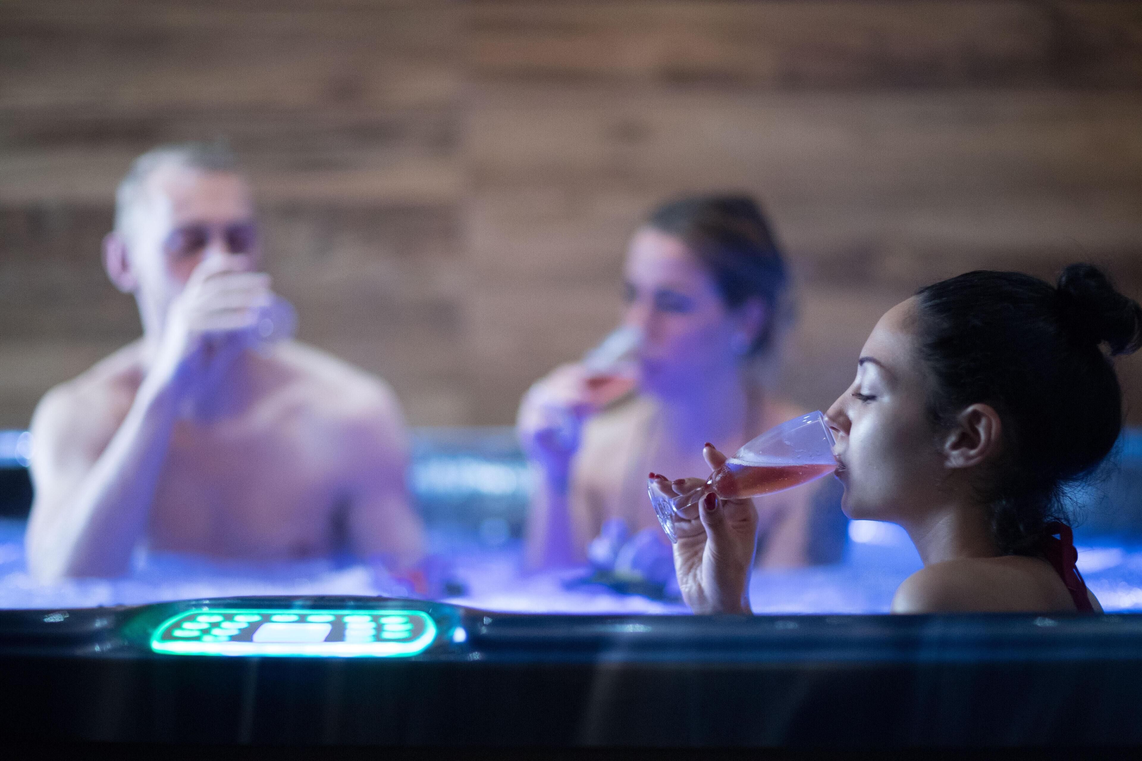 Un jacuzzi con pantalla digital, tres personas y un fondo de pared de madera.