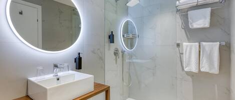 A modern bathroom with a white sink, two mirrors, a glass-enclosed shower, and white towels on a rack.