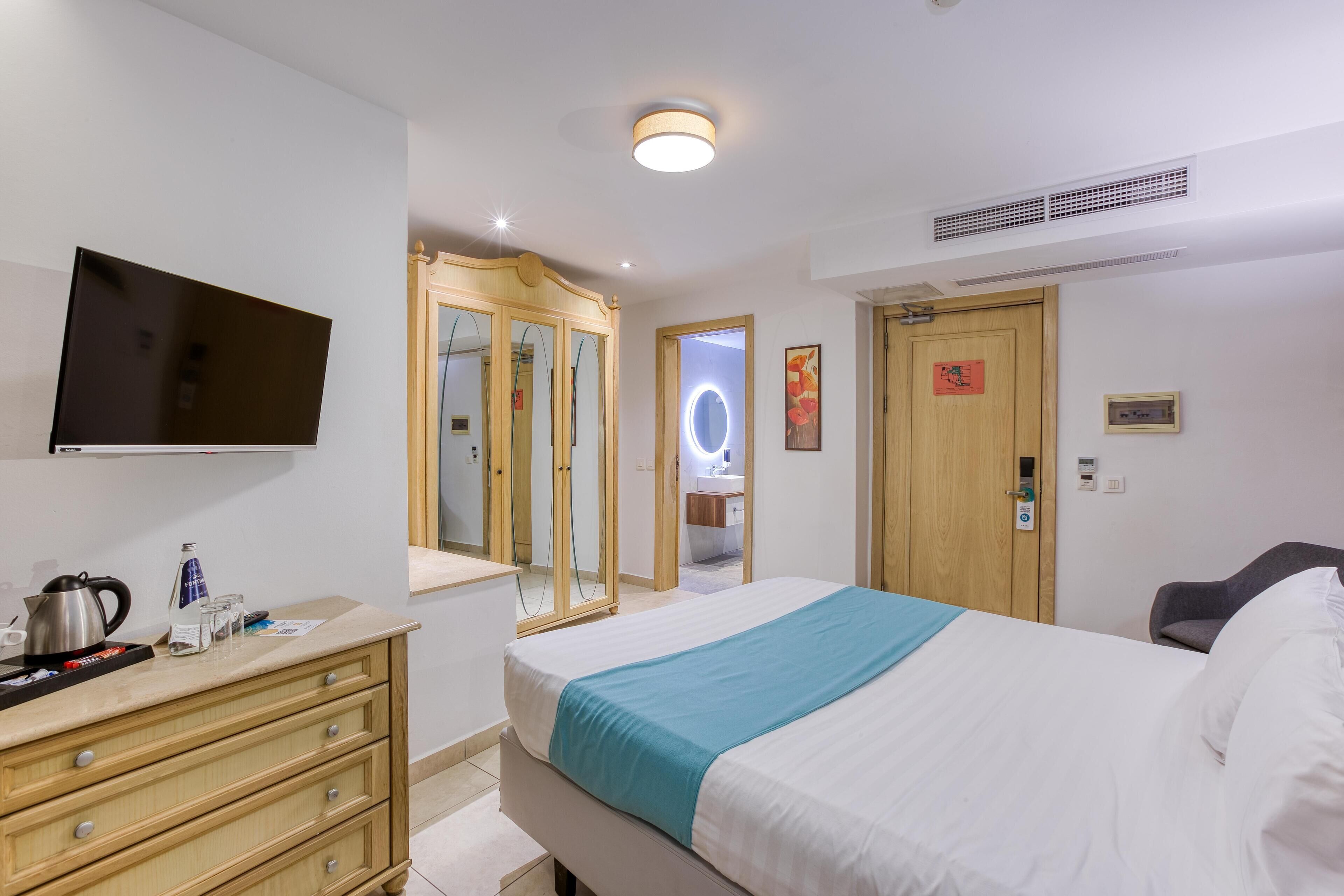 A hotel room with a bed, a TV, a dresser, a mirror, and a door with a sign.