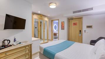 A hotel room with a bed, a TV, a dresser, a mirror, and a door with a sign.