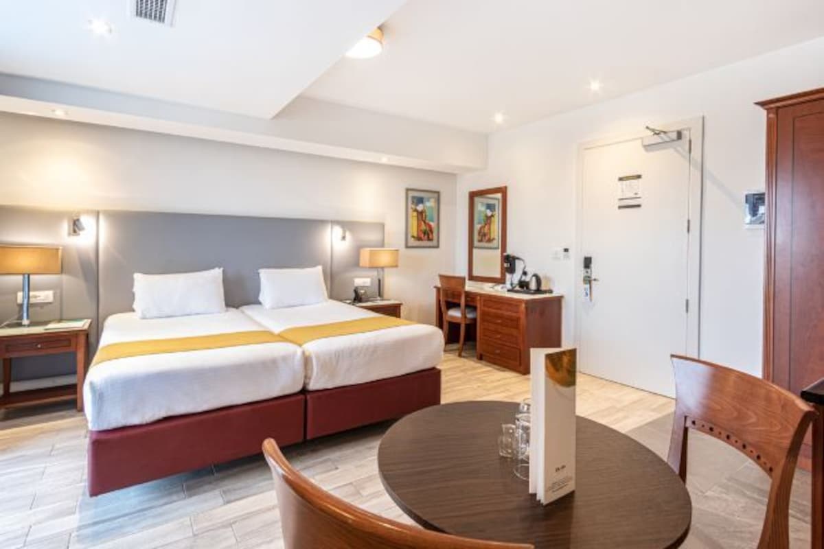 A hotel room with a double bed, a desk, a chair, a round table, and a wardrobe.
