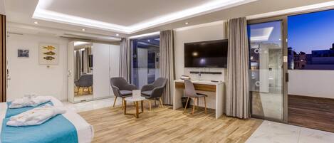 A modern hotel room with a bed, desk, chairs, and a TV.