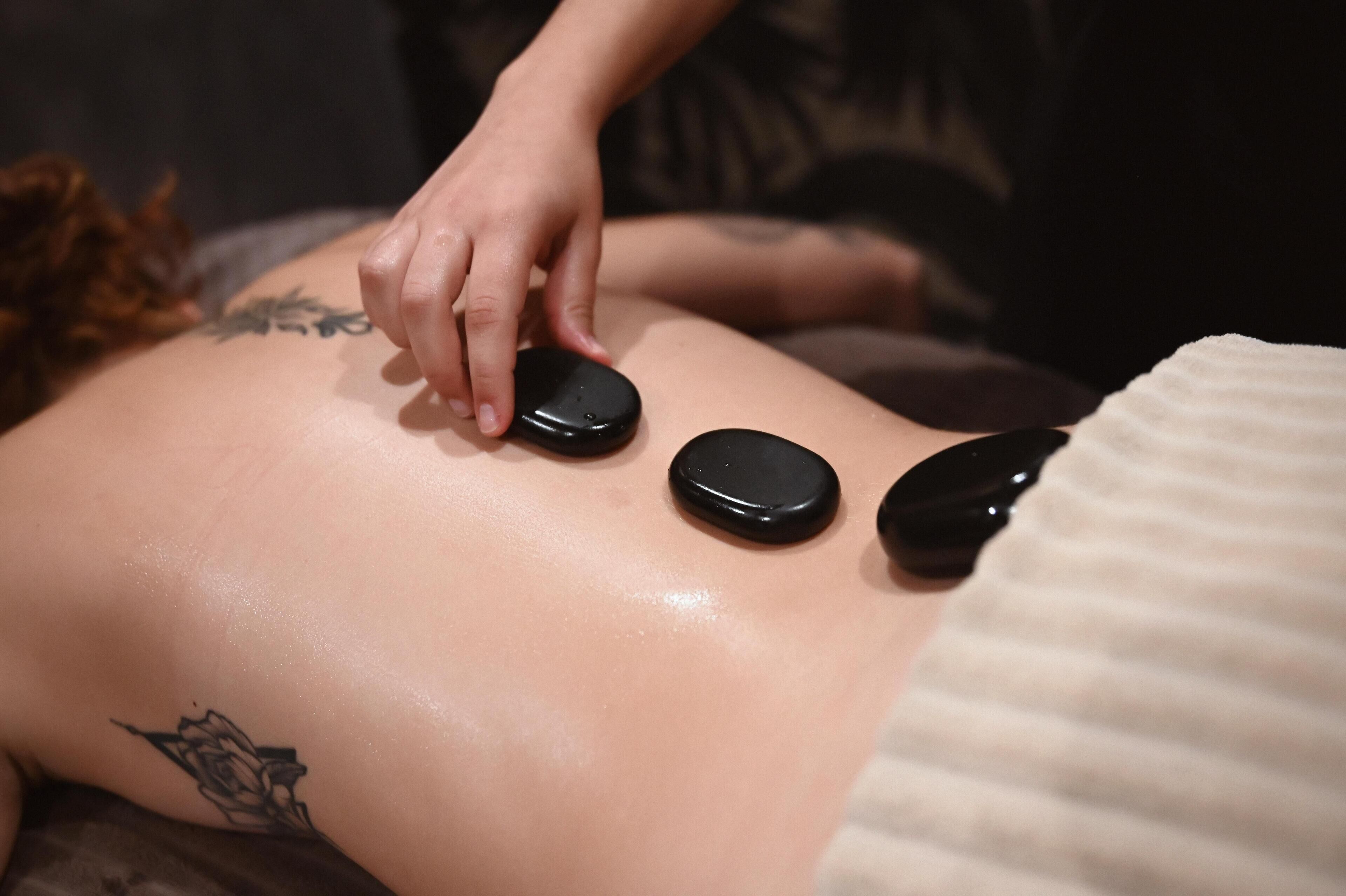 Une personne reçoit un massage du dos, avec trois pierres noires placées sur son dos.