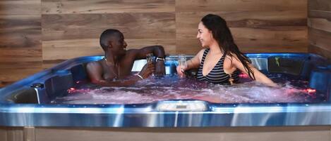 A hot tub with two people, wooden walls, and decorative vases.
