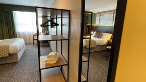 Habitación de hotel con dos camas, un espejo, un estante con toallas y vistas al exterior.