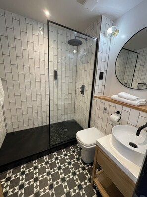 A modern bathroom with a glass-enclosed shower, a white toilet, a sink with a mirror, and patterned floor tiles. - Hotel Nineteen (Barnsley)