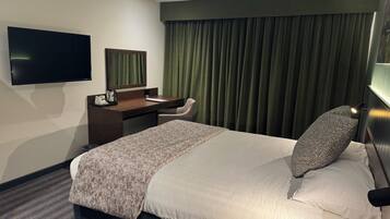 A hotel room with a bed, a desk, a chair, a television, and a window with curtains.