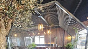 Un rincón de descanso acogedor y moderno, con una mesa de madera y bancos acolchados, rodeado de paneles de madera y un techo de malla.