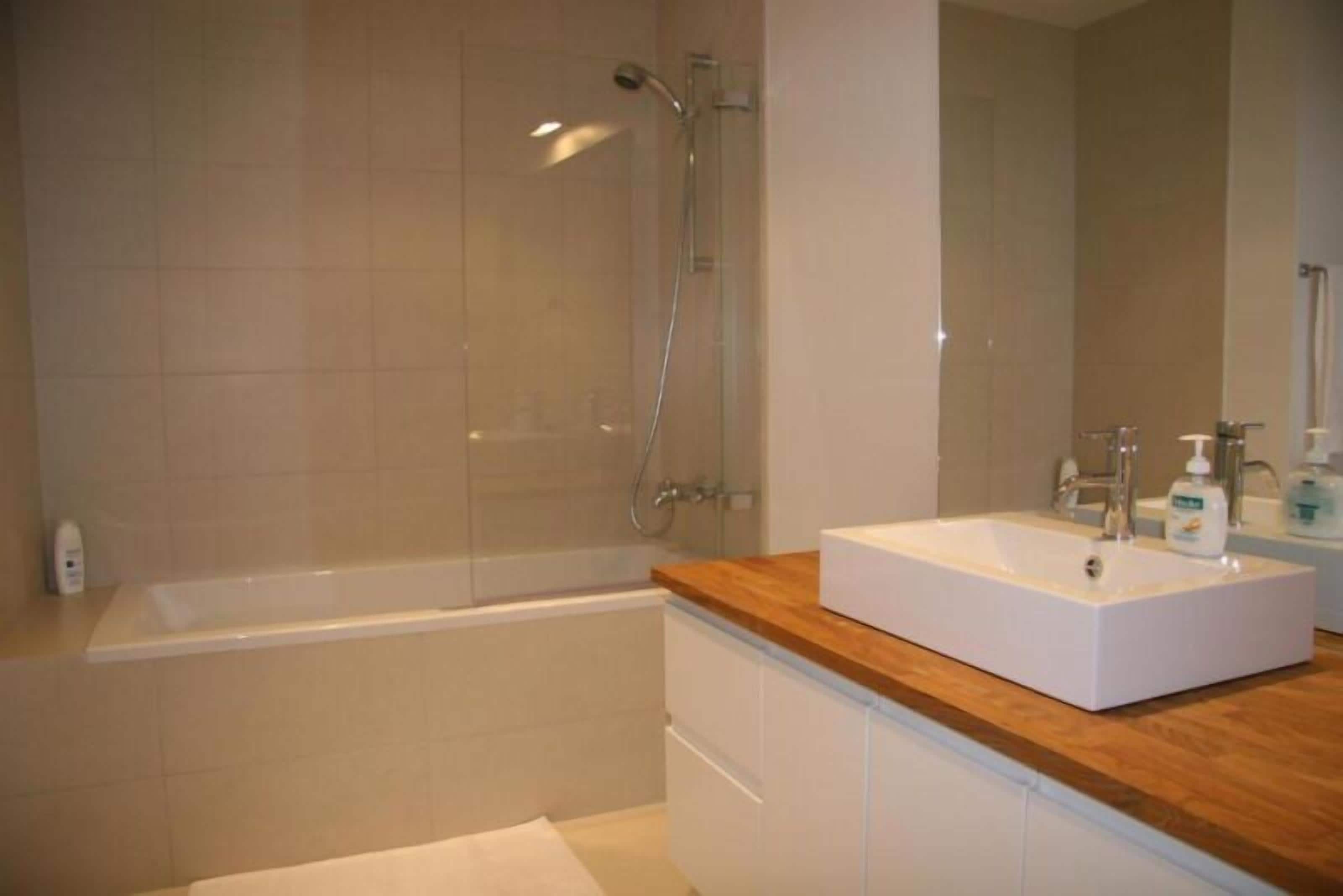 A bathroom with a bathtub, a wooden vanity, a mirror, and a shower.