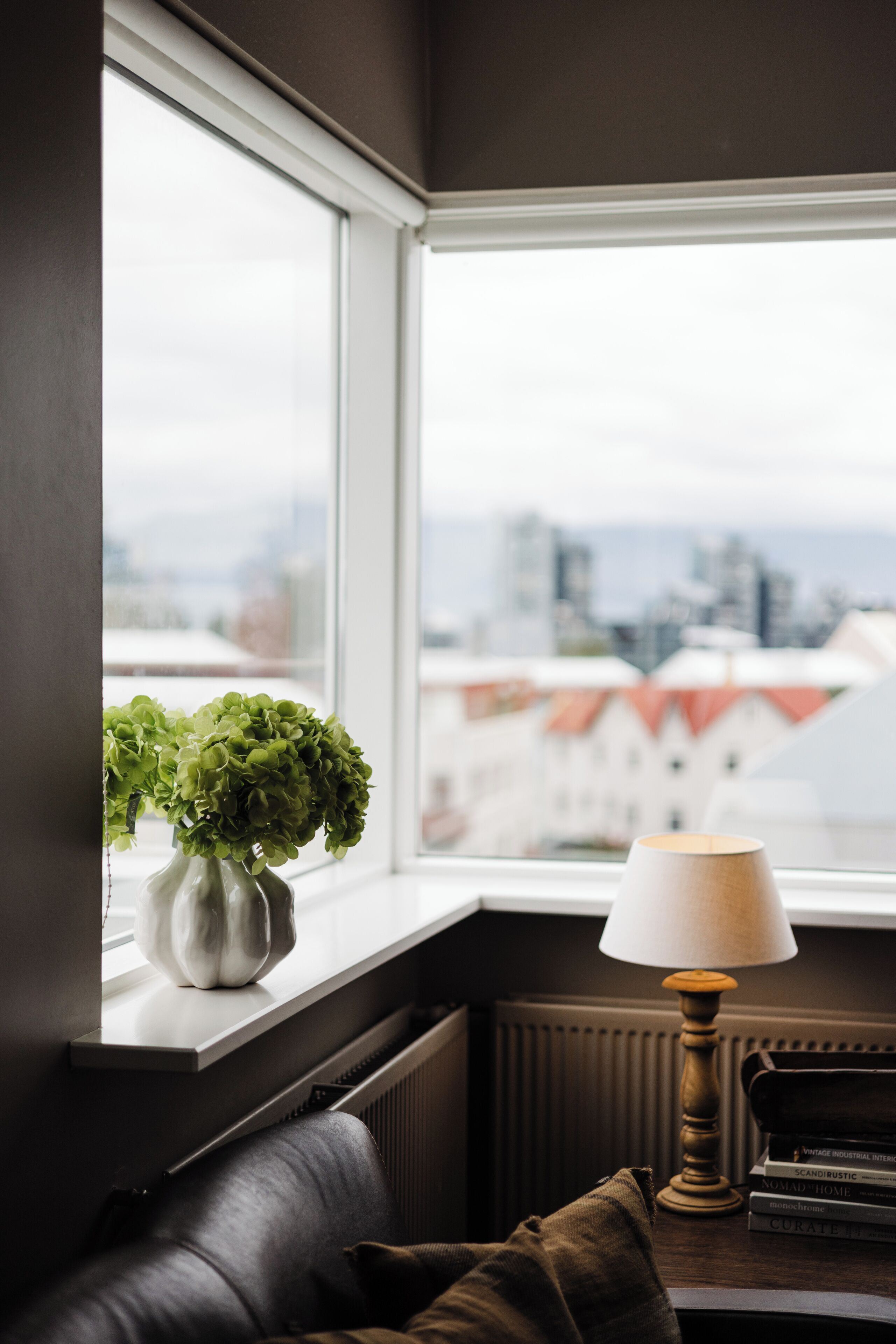 Un rincón acogedor con una ventana, un florero con plantas verdes, una lámpara y un sofá de cuero.