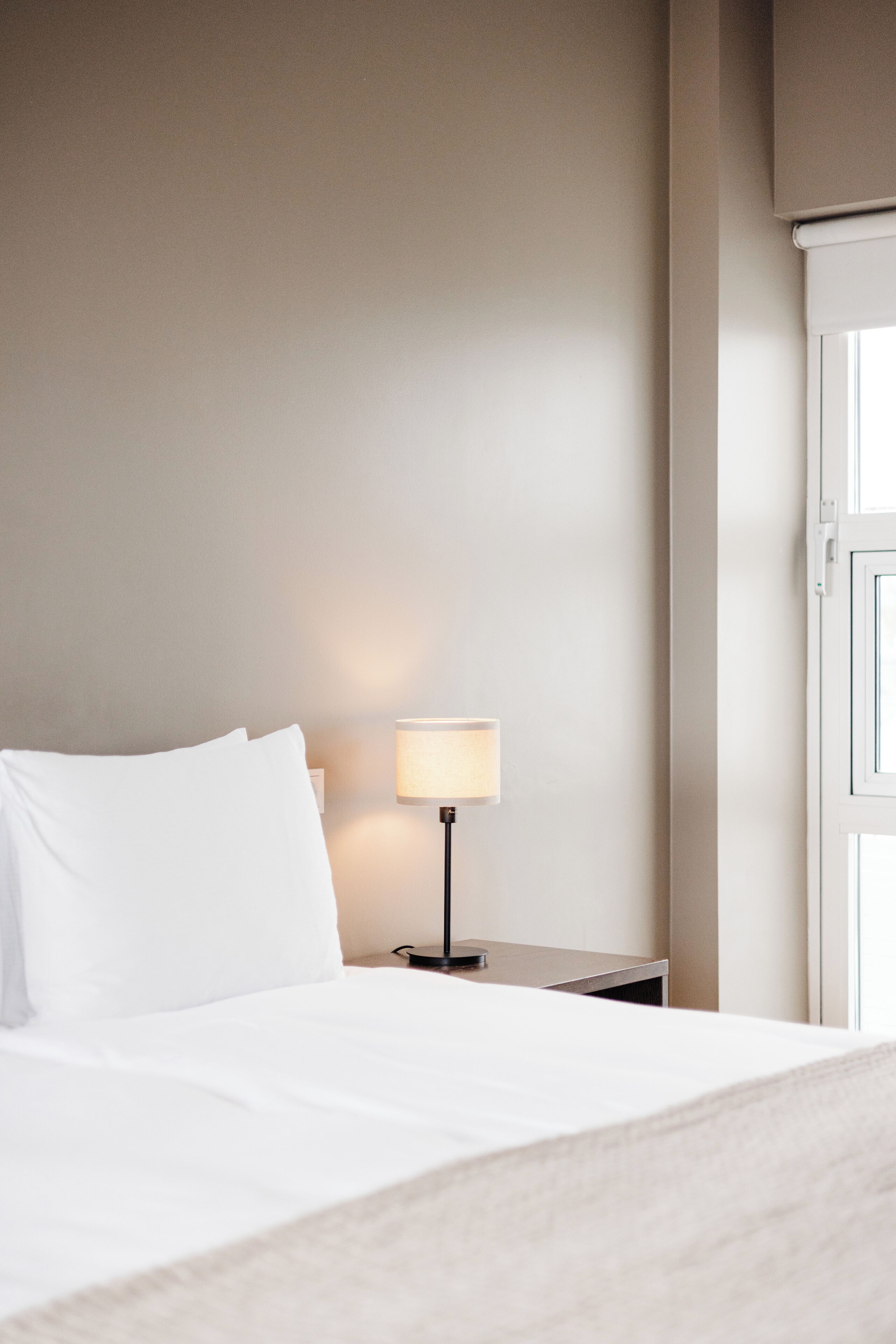 A neatly made bed with white linens, a bedside lamp, and a closed door in a hotel room.