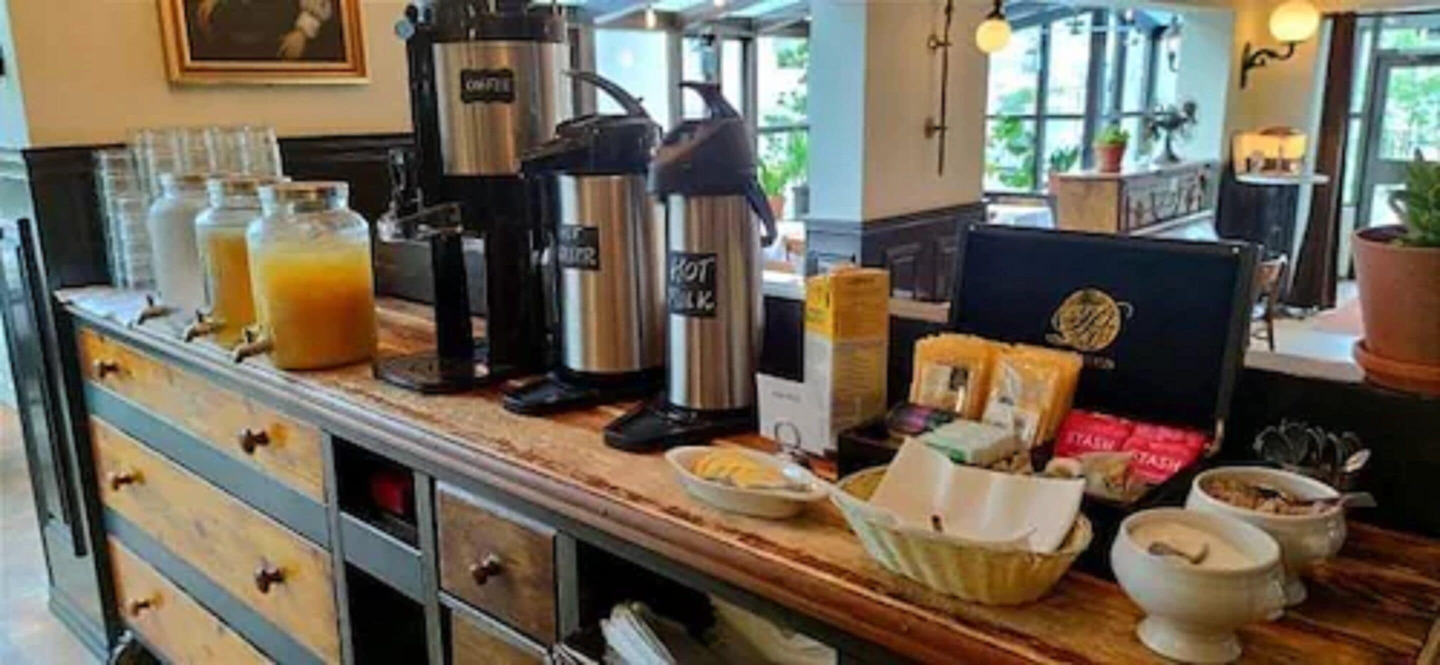 A breakfast bar with coffee makers, a fruit juice dispenser, and various breakfast items.