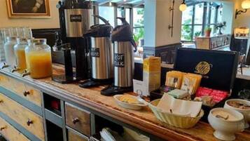 A breakfast bar with coffee makers, a fruit juice dispenser, and various breakfast items.