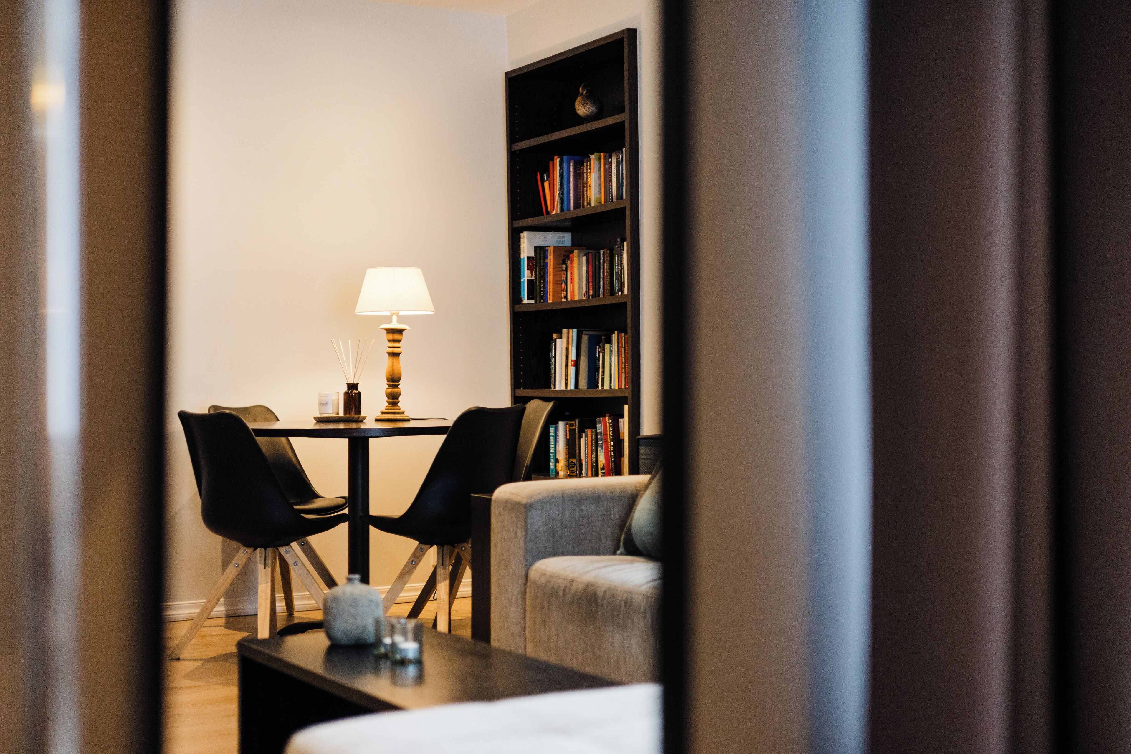 A modern living room with a dining area, featuring a bookshelf, a lamp, and a sofa.