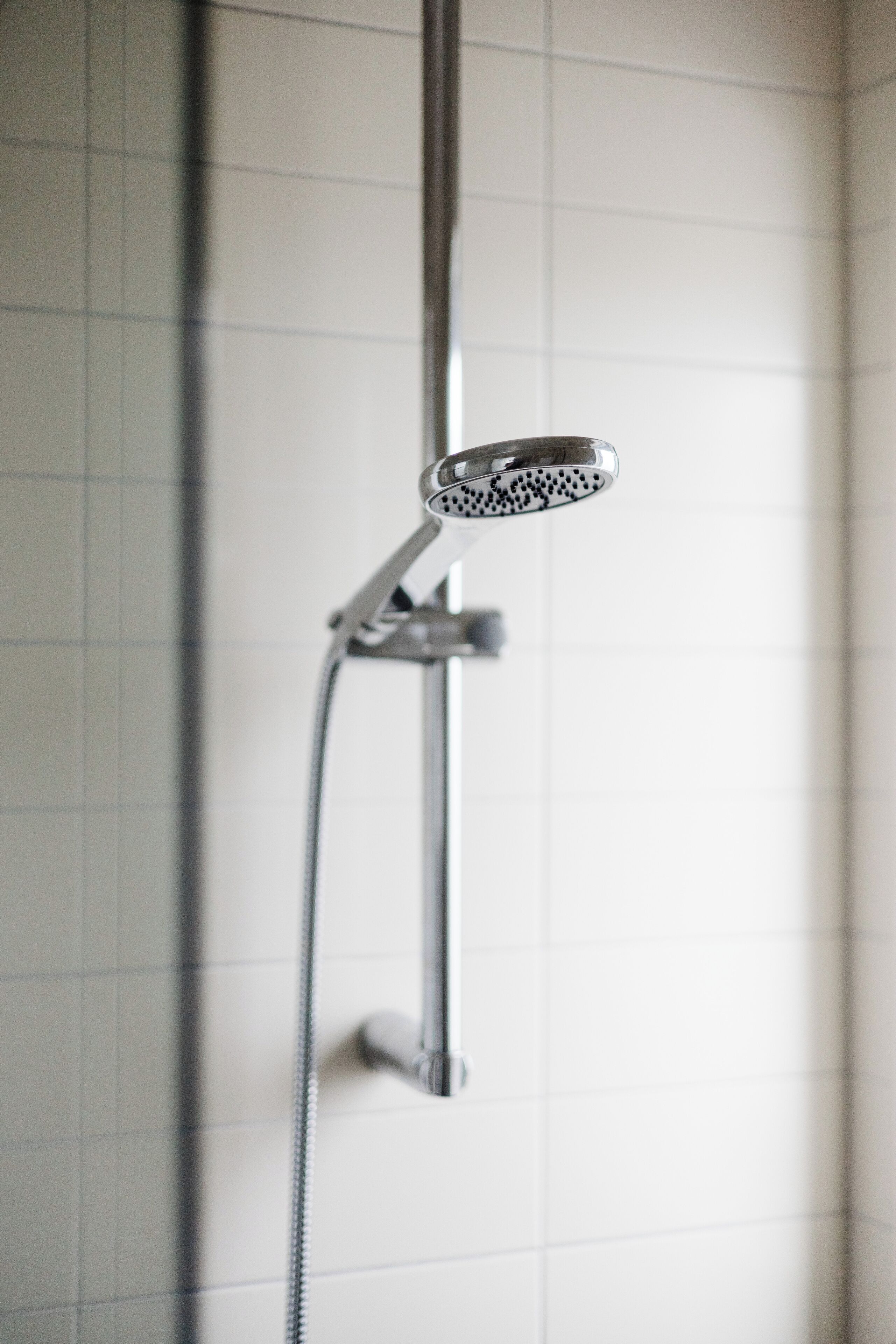 Un pommeau de douche doté d’un flexible, fixé au mur et présentant un motif quadrillé.