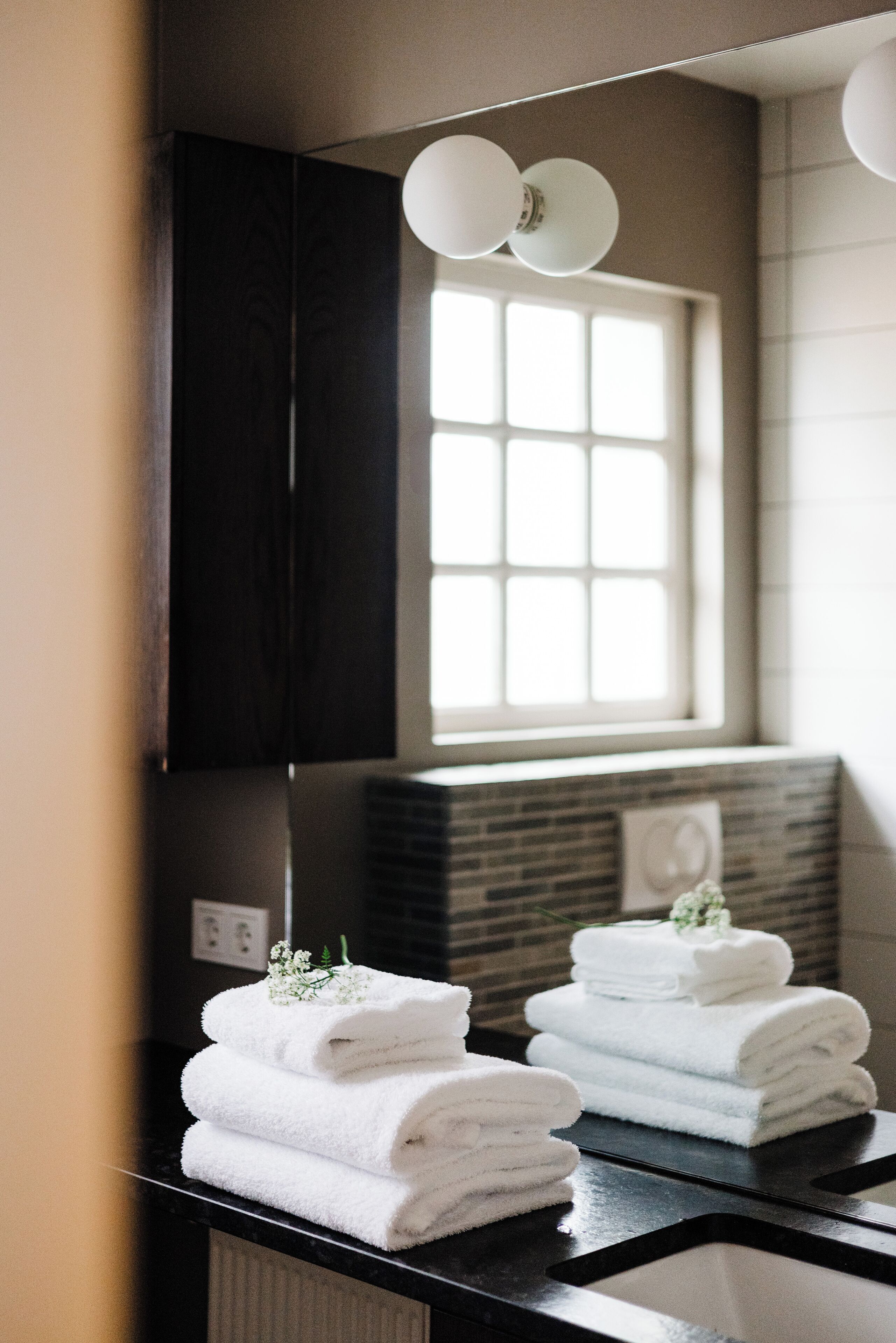 A bathroom with a mirror, a window, and a stack of white towels.