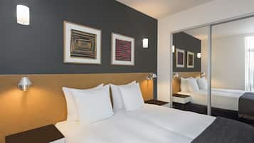 A hotel room with a large bed, a headboard, two framed artworks, a nightstand, a lamp, and a mirror.
