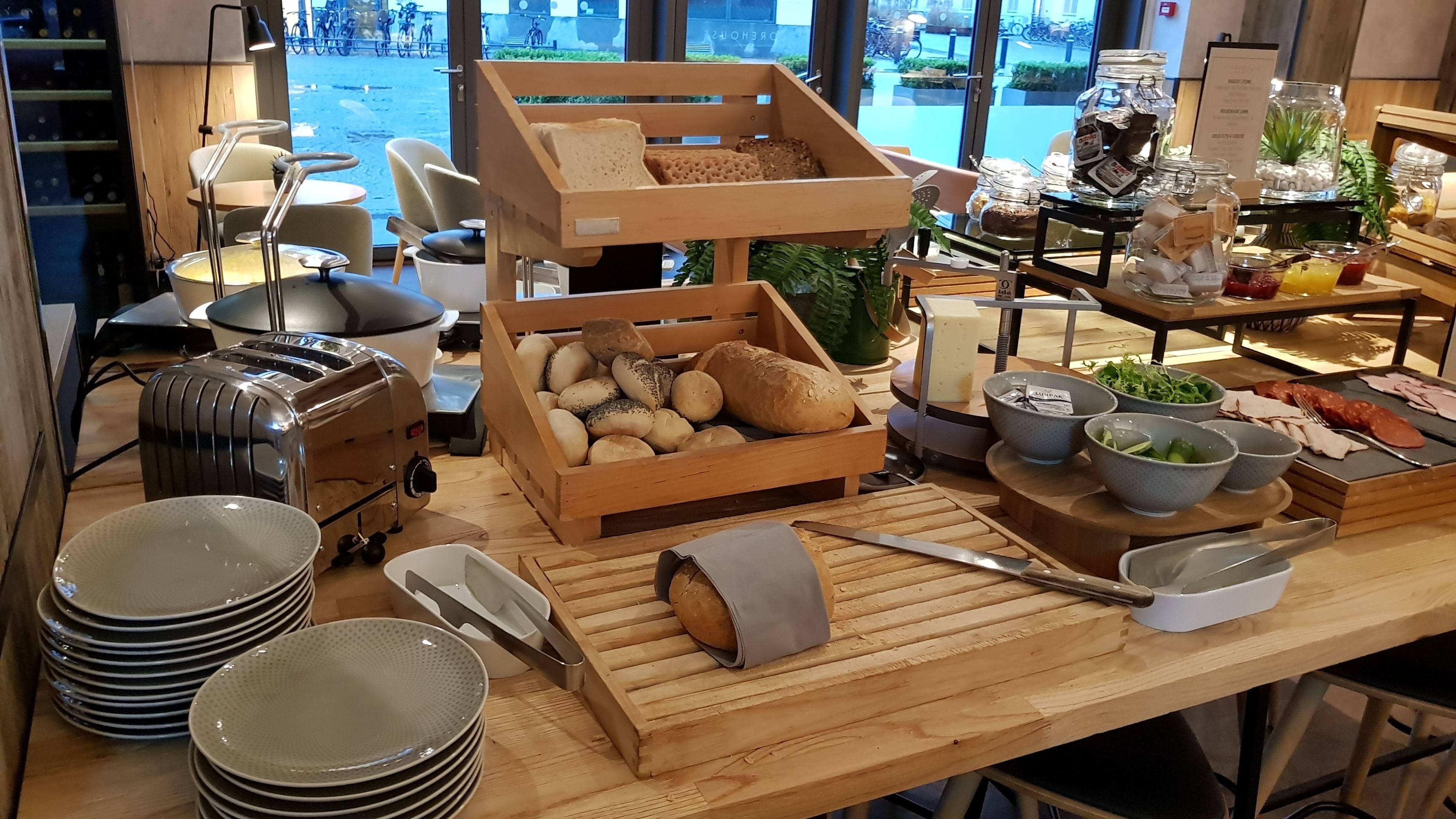 A breakfast buffet setup with bread, pastries, and various breakfast items on a wooden table.