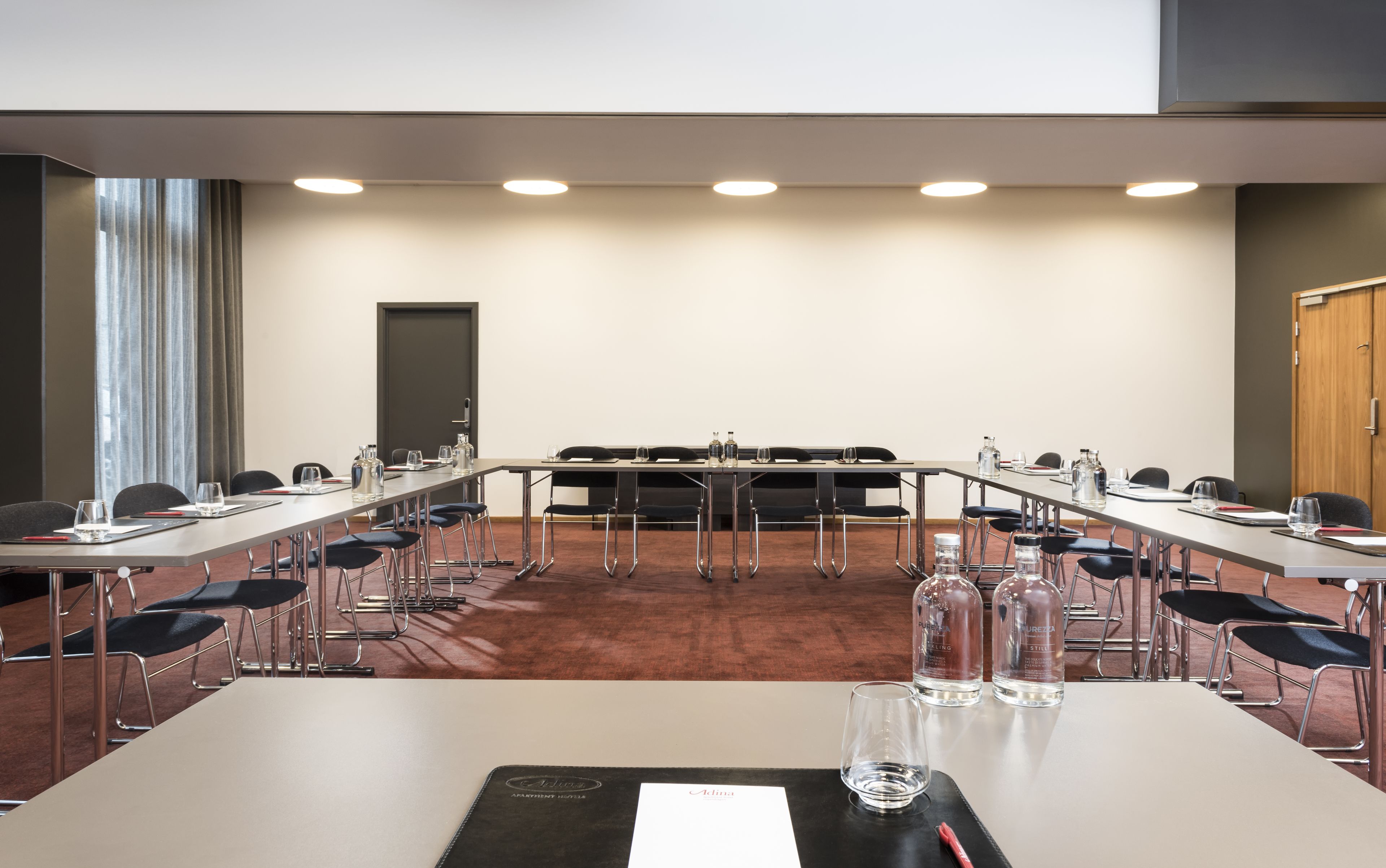 Ein Konferenzraum mit einem langen Tisch, Stühlen und einer Tür.