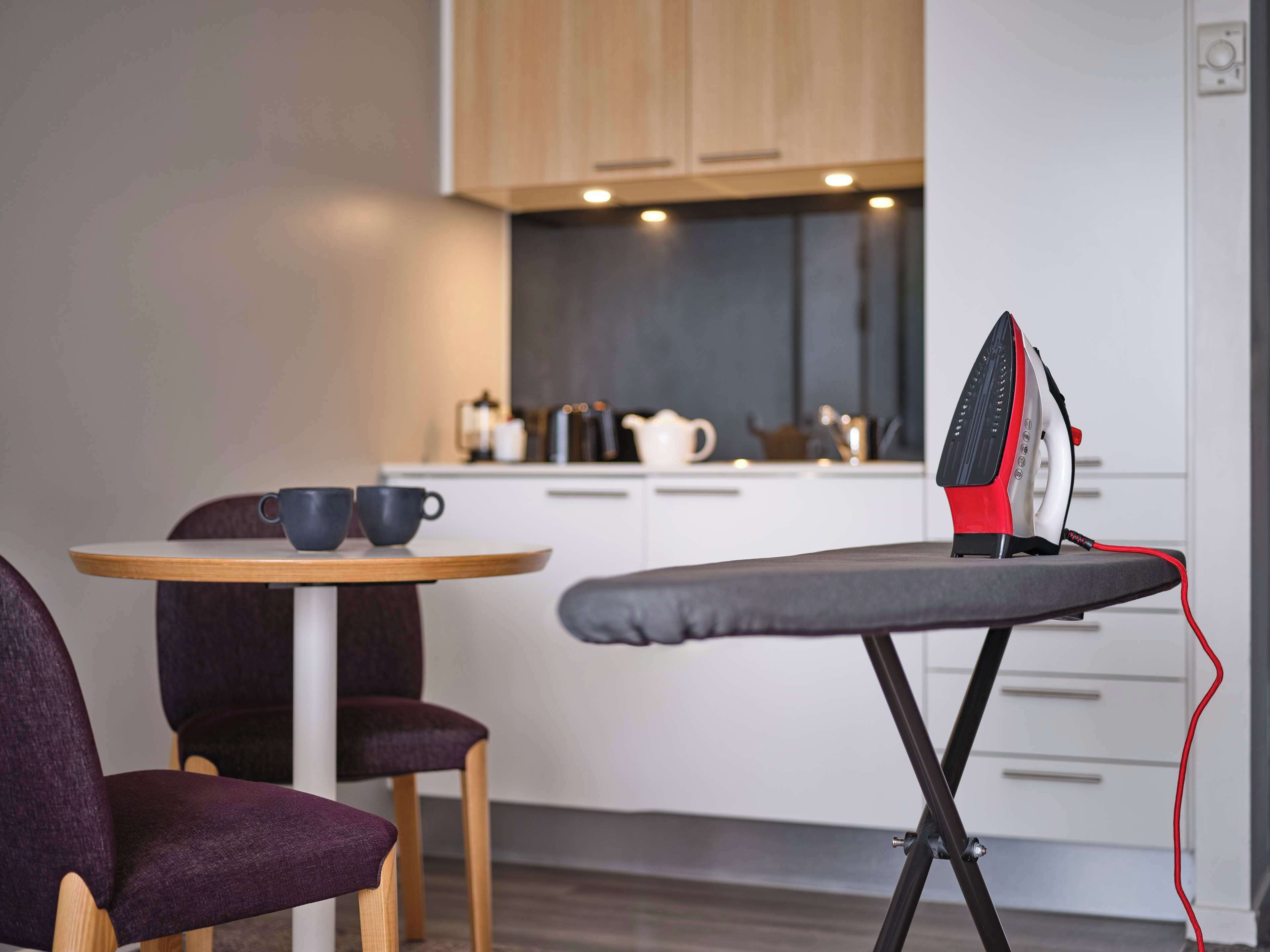 Une cuisine moderne avec des meubles en bois, une table de salle à manger ronde accompagnée de deux chaises, et une planche à repasser avec un fer à repasser.