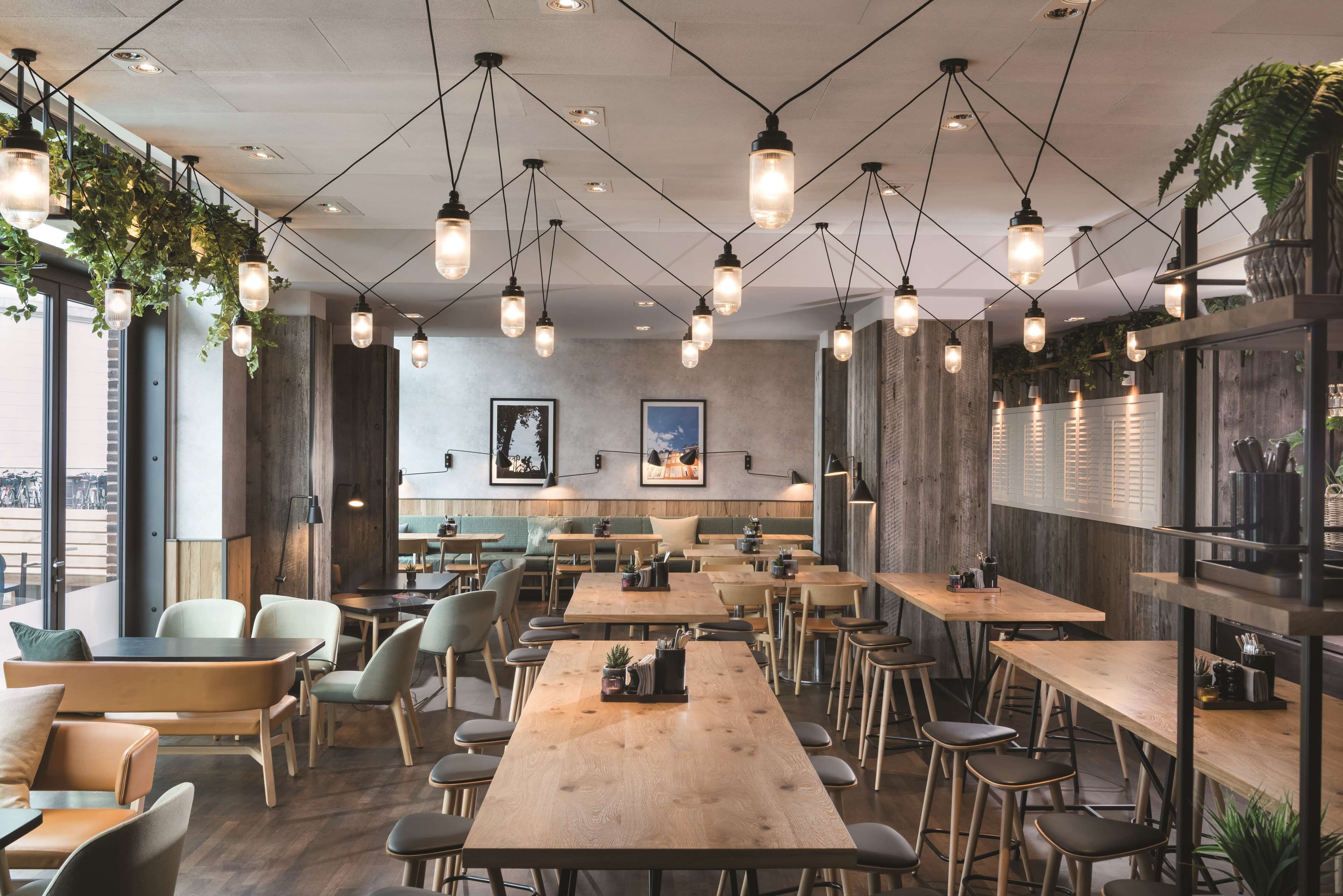 Un ristorante moderno con tavoli e sedie in legno, lampade a sospensione e ampie finestre.