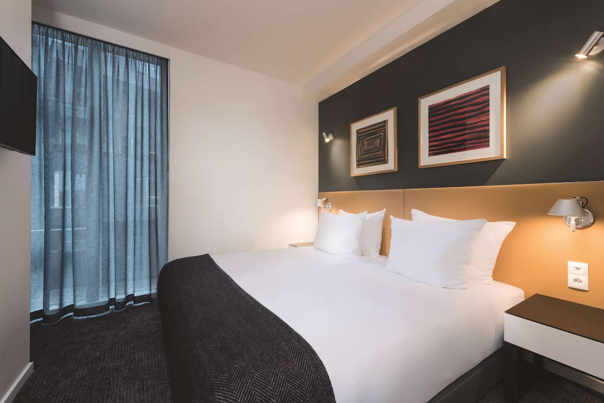 Ein Hotelzimmer mit einem großen Bett, einem Kopfteil, einem Nachttisch, einer Lampe und zwei gerahmten Bildern an der Wand.
