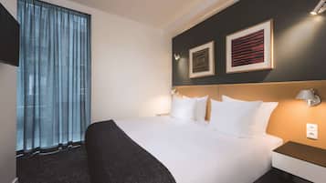 Ein Hotelzimmer mit einem großen Bett, einem Kopfteil, einem Nachttisch, einer Lampe und zwei gerahmten Bildern an der Wand.