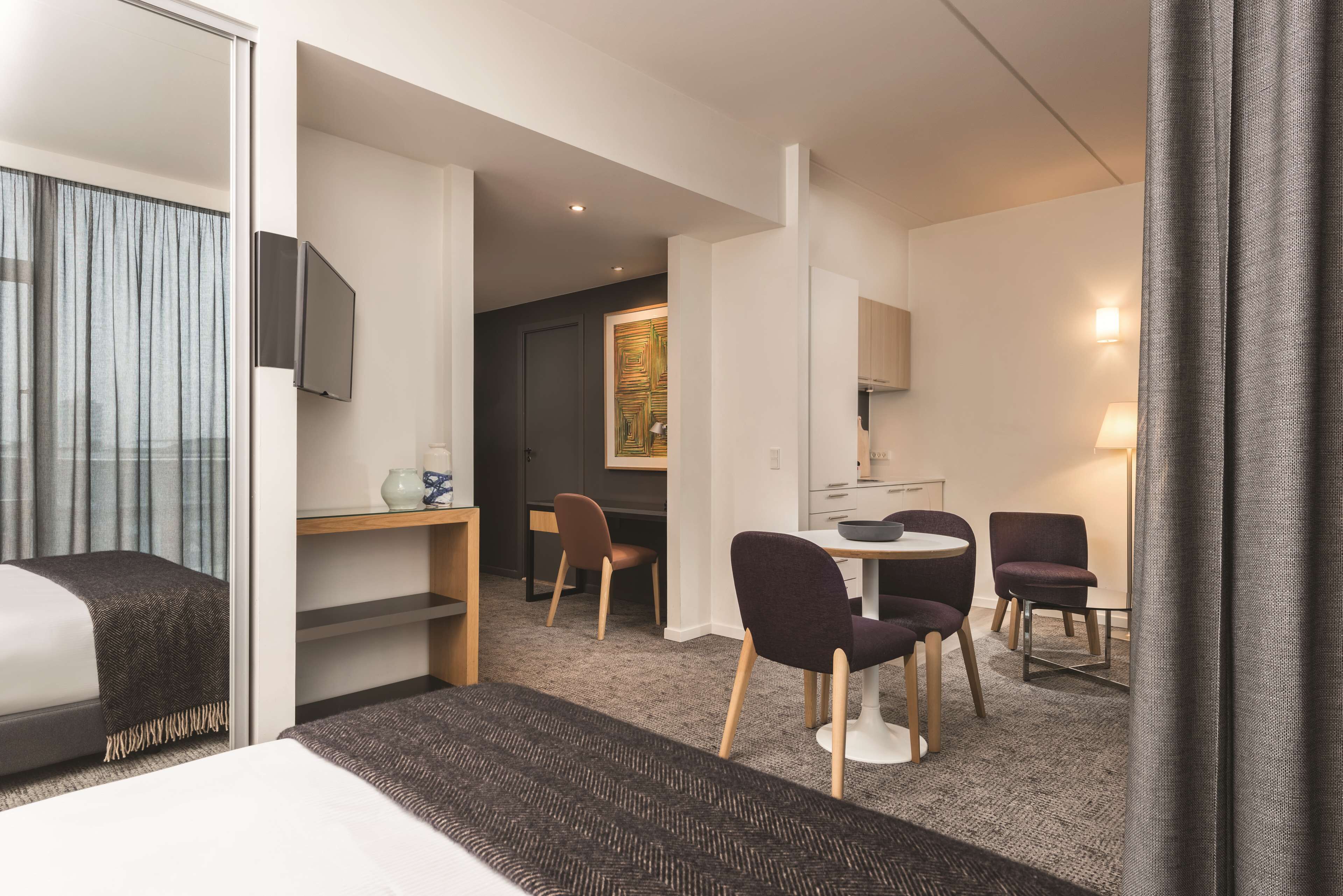 A hotel room with a bed, a desk, two chairs, a small table, and a TV.