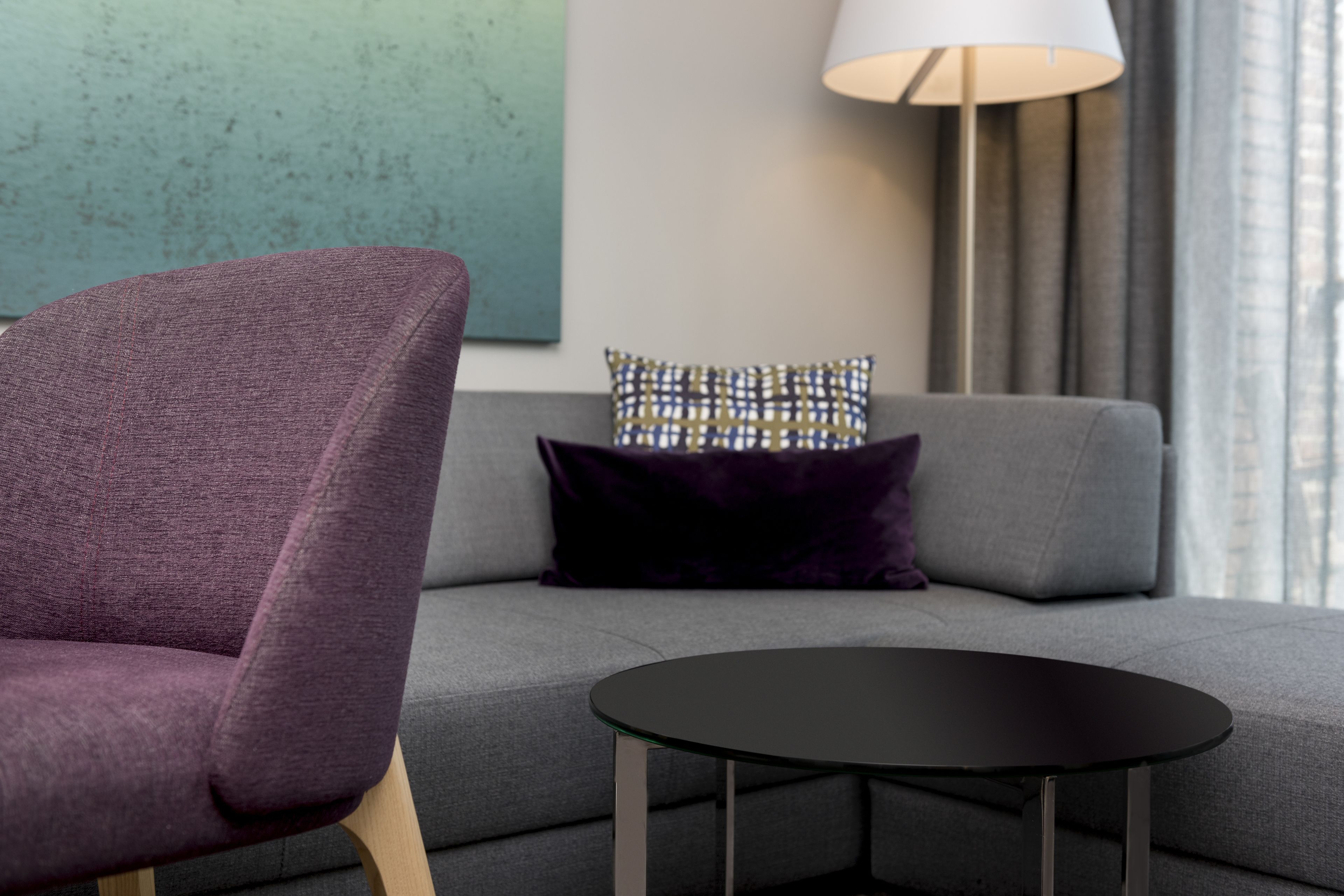 Un salon moderne avec un fauteuil violet, un canapé gris, une table ronde noire et un coussin à motifs.