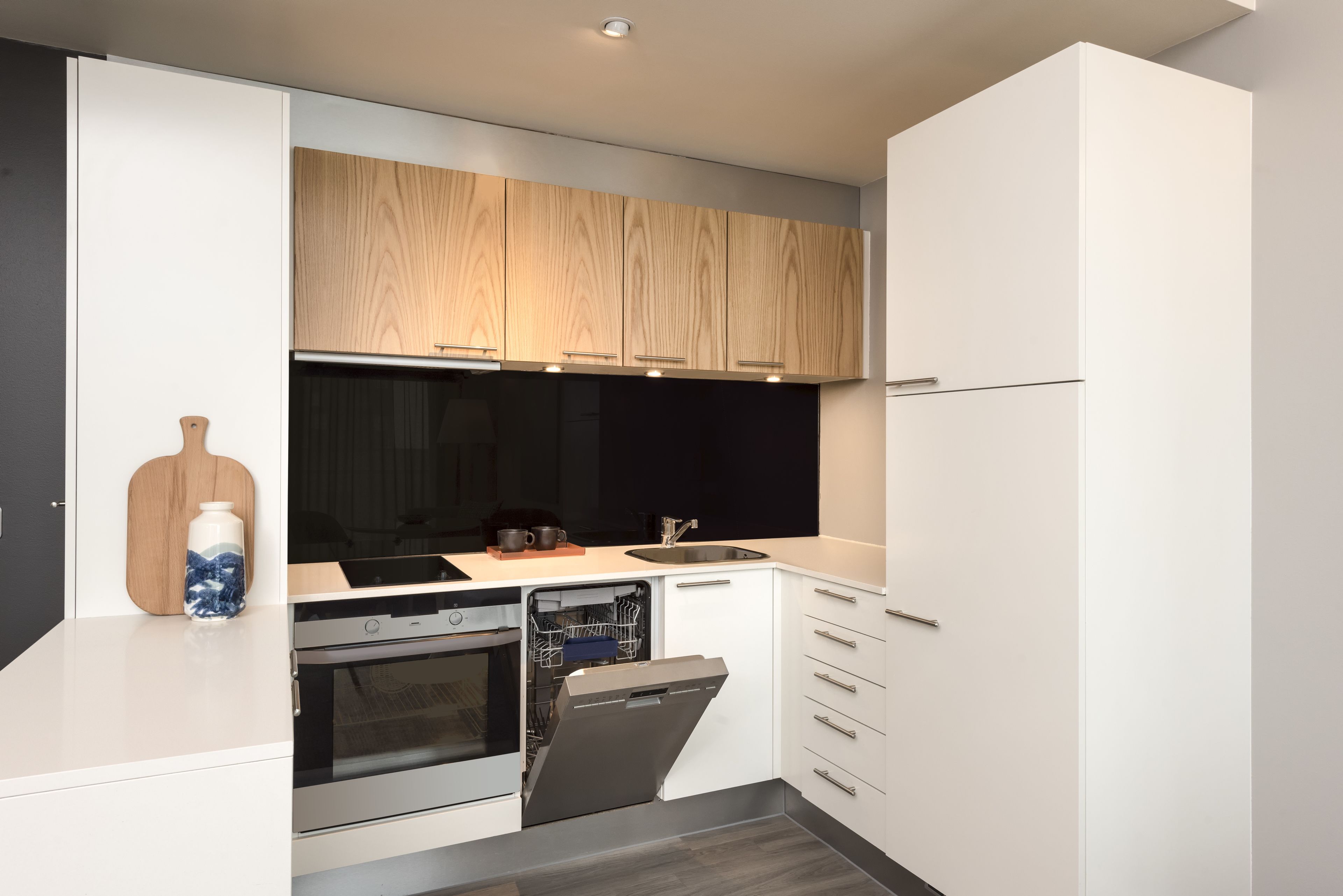 A modern kitchen with white cabinetry, a built-in oven, a dishwasher, and a wooden backsplash.