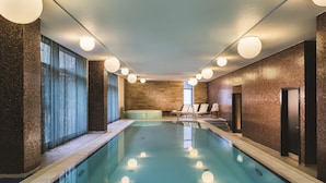 Una piscina con piso de baldosas, un jacuzzi y sillas de descanso.