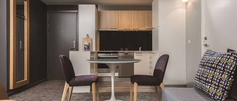 A compact living space with a kitchenette, two purple chairs, a round table, and a grey sofa.