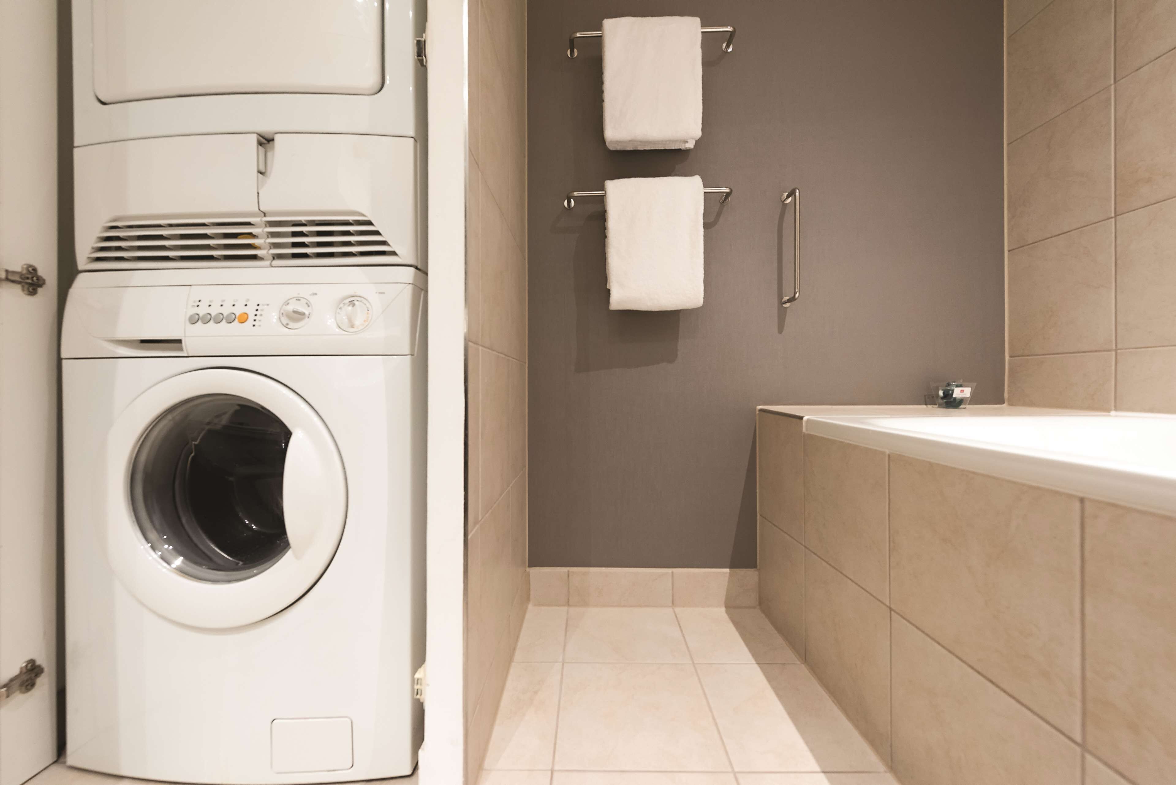 A compact, modern bathroom with a built-in washer and dryer, a bathtub, and two towel racks.