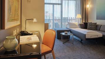 Une chambre d’hôtel équipée d’un bureau, d’une chaise, d’un canapé et d’une petite table sur laquelle se trouvent un bol et un verre.